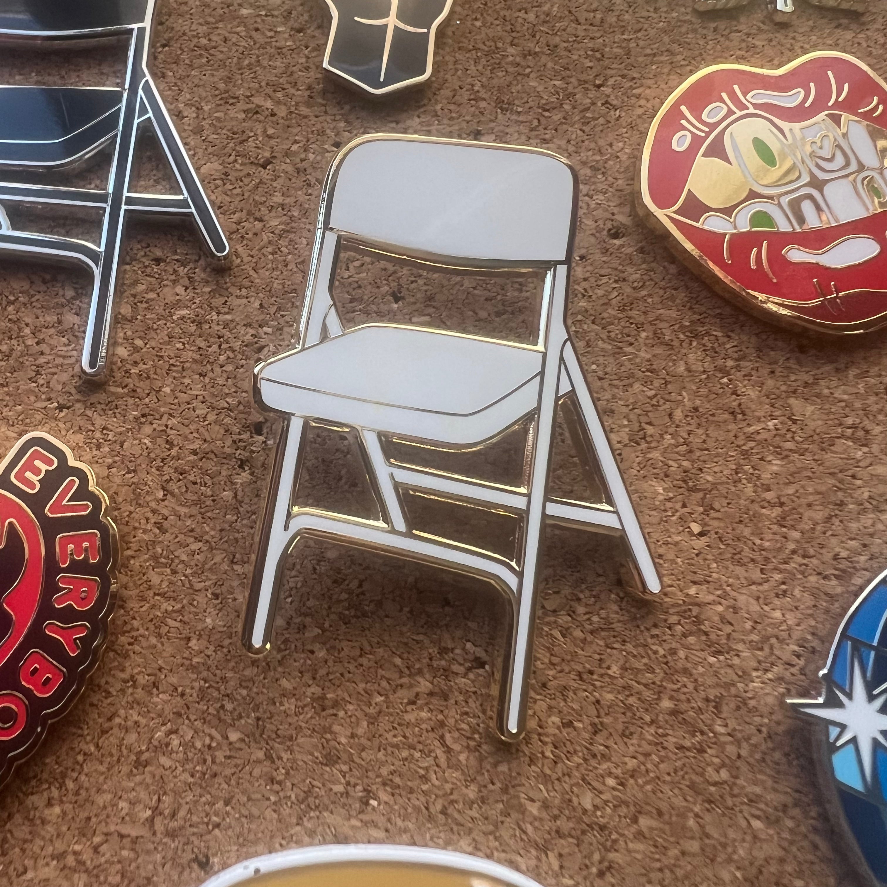Pin with a white chair design on a cork board with other pins around