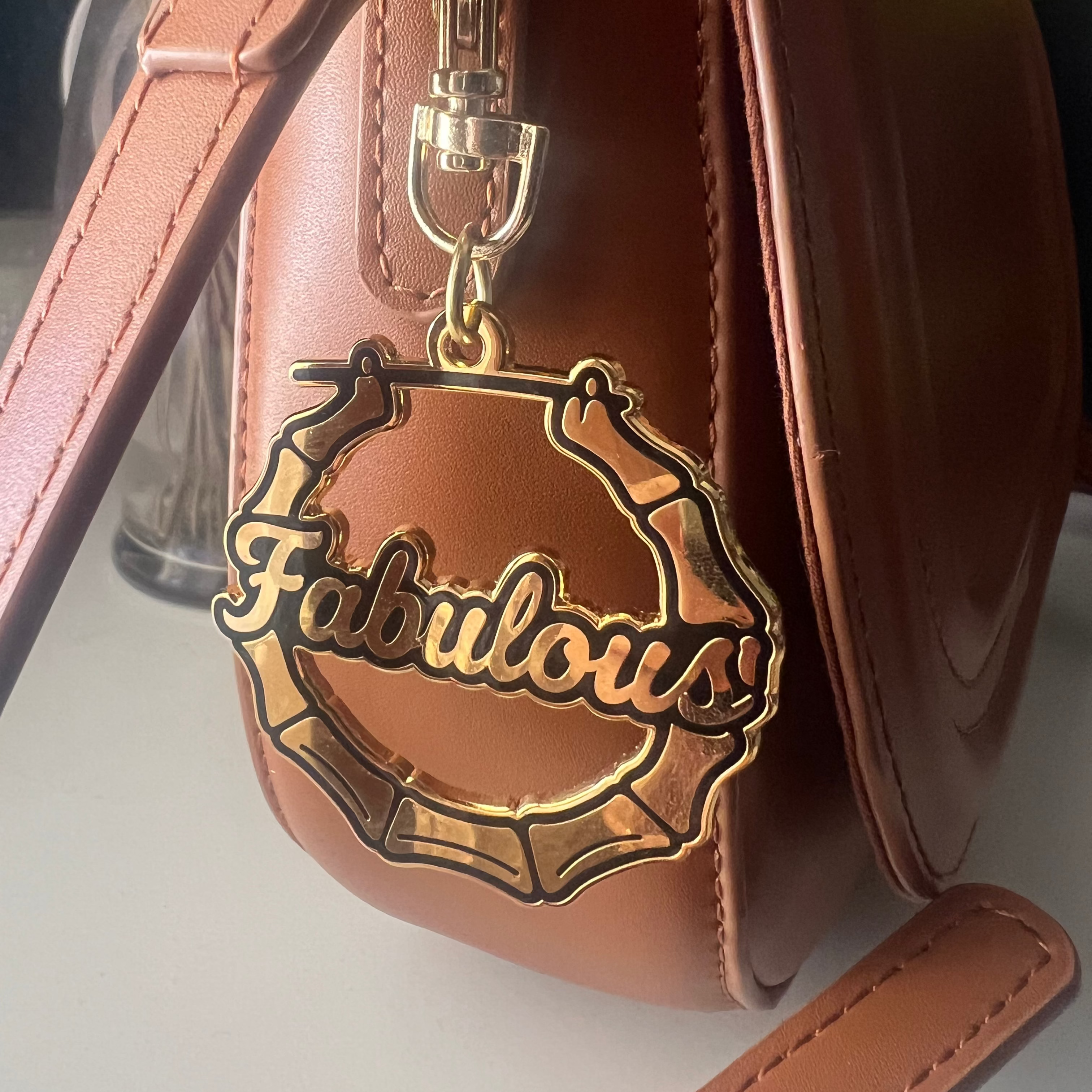 Brown leather bag with a 'Fabulous' keychain on a light background