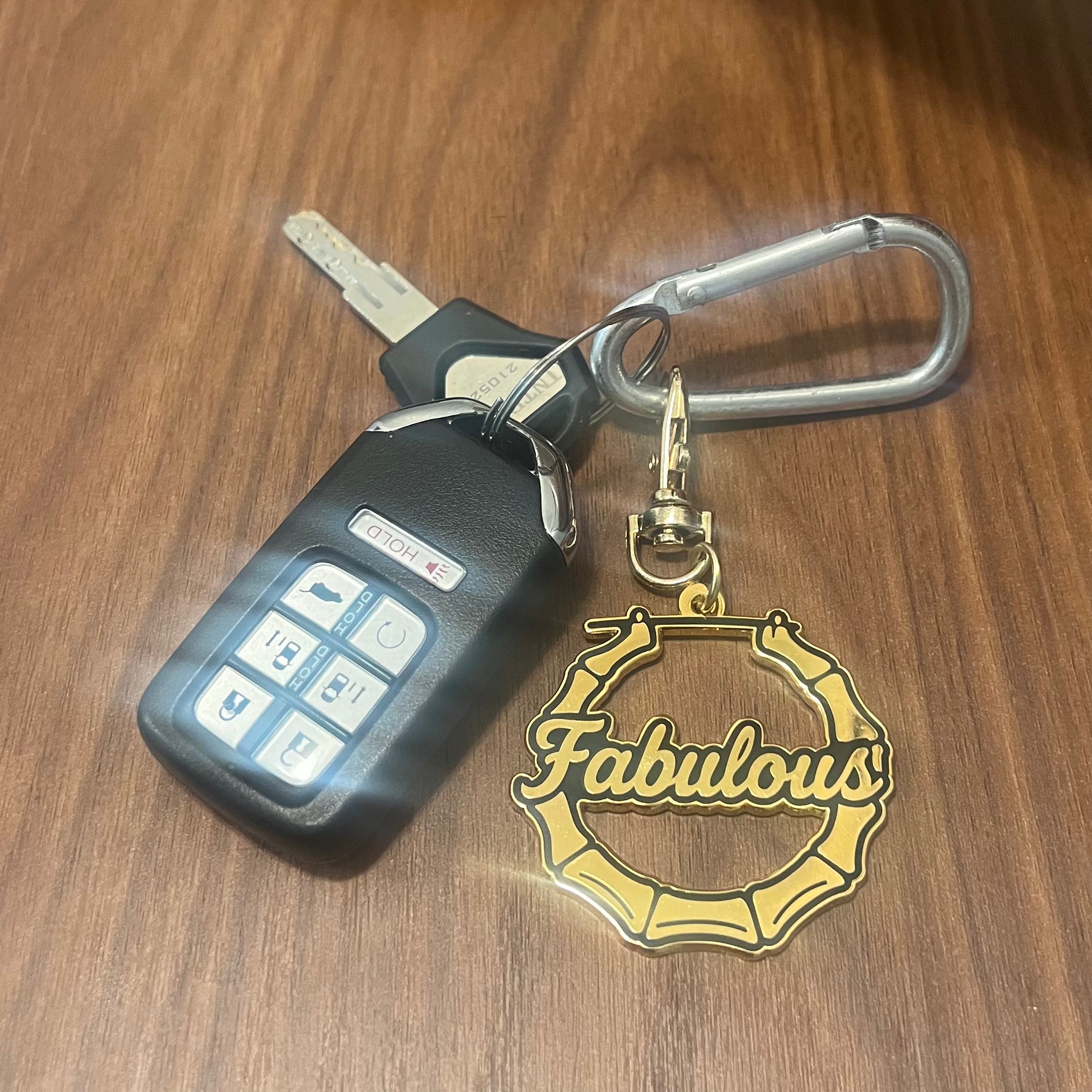 Keychain with a car key fob and 'Fabulous' charm on a wooden surface