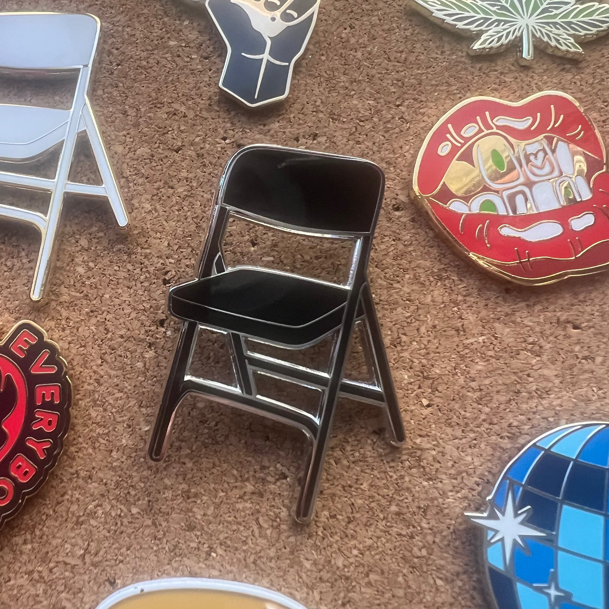 Black folding chair surrounded by various colorful pins on a cork board