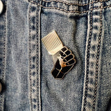 Pin with a raised fist design on a denim jacket
