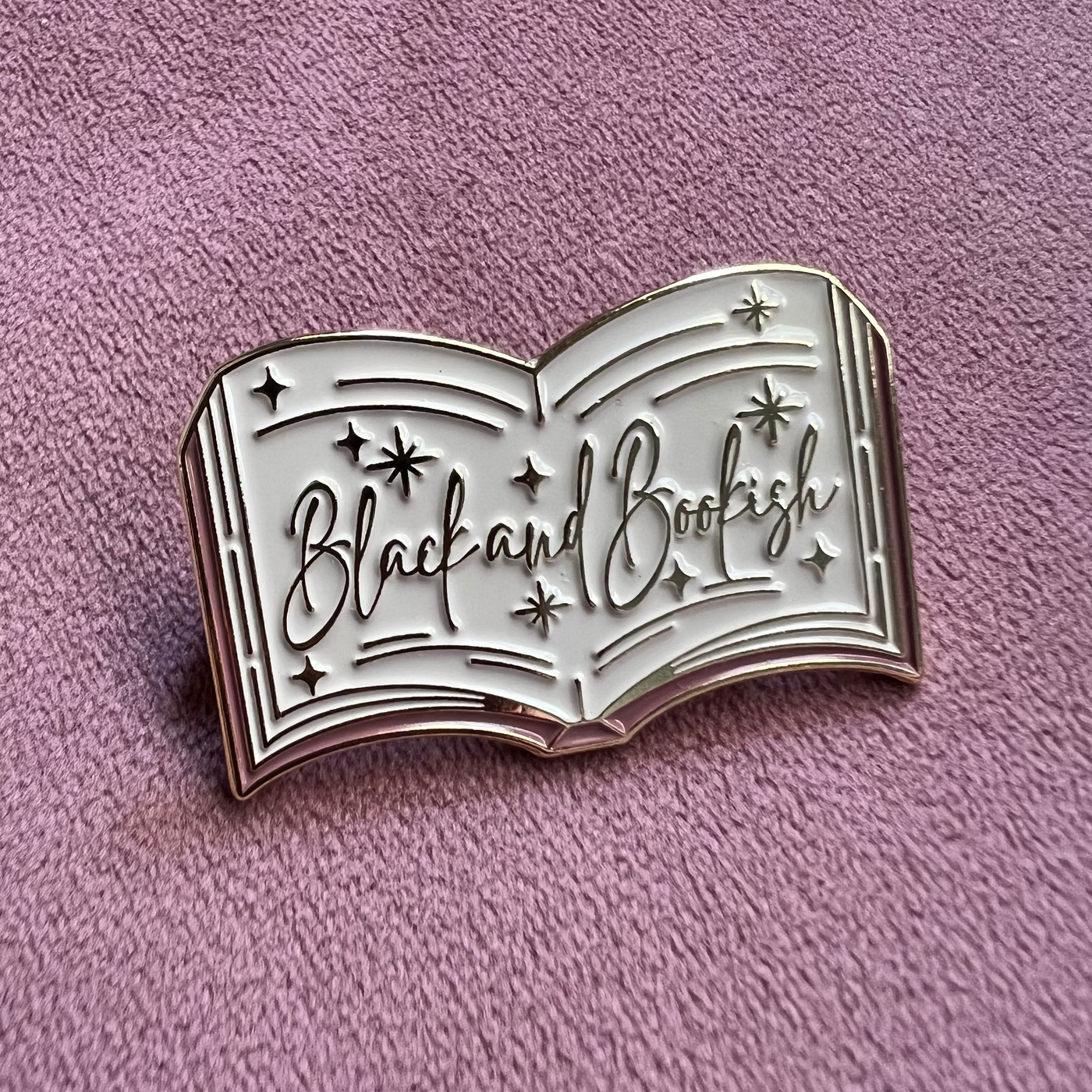 Metallic book-shaped pin with 'Black and Bookish' text on a pink background