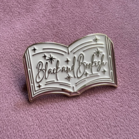 Metallic book-shaped pin with 'Black and Bookish' text on a pink background