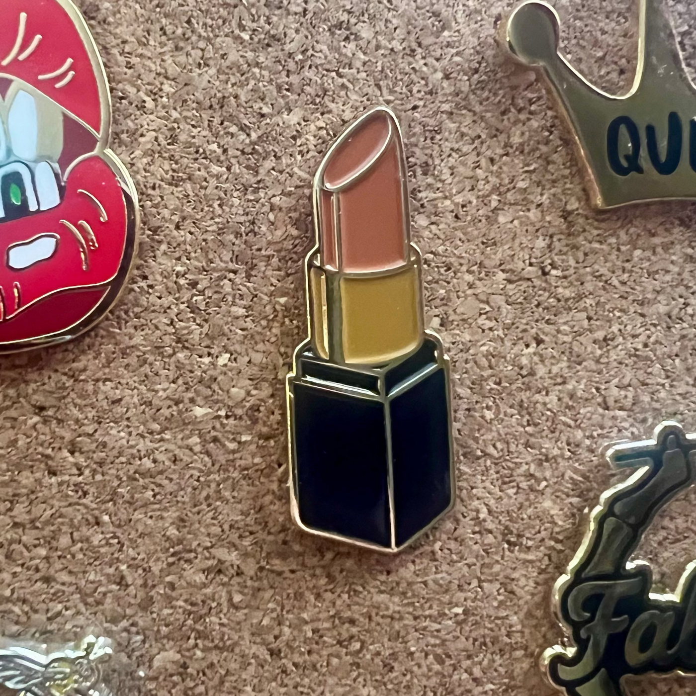 Collection of various pins including a lipstick, car, and 'Queen' design on a textured surface.