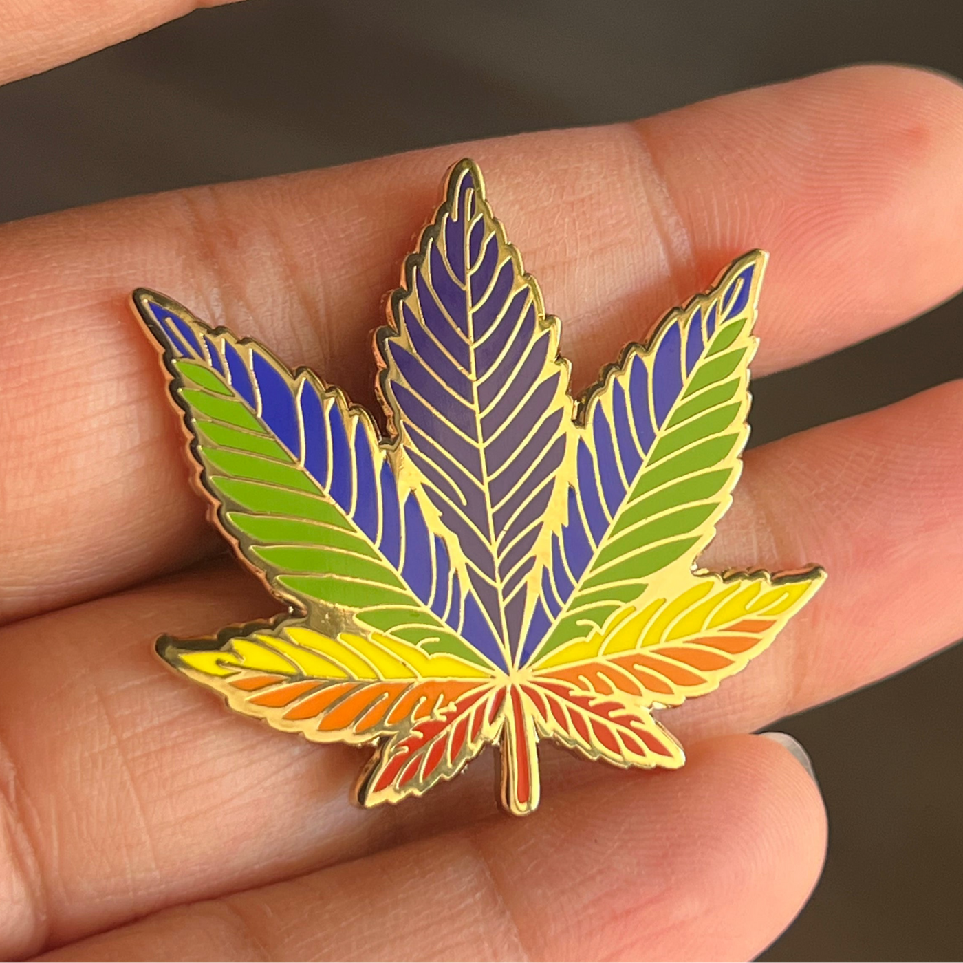 Colorful cannabis leaf-shaped pin held between fingers