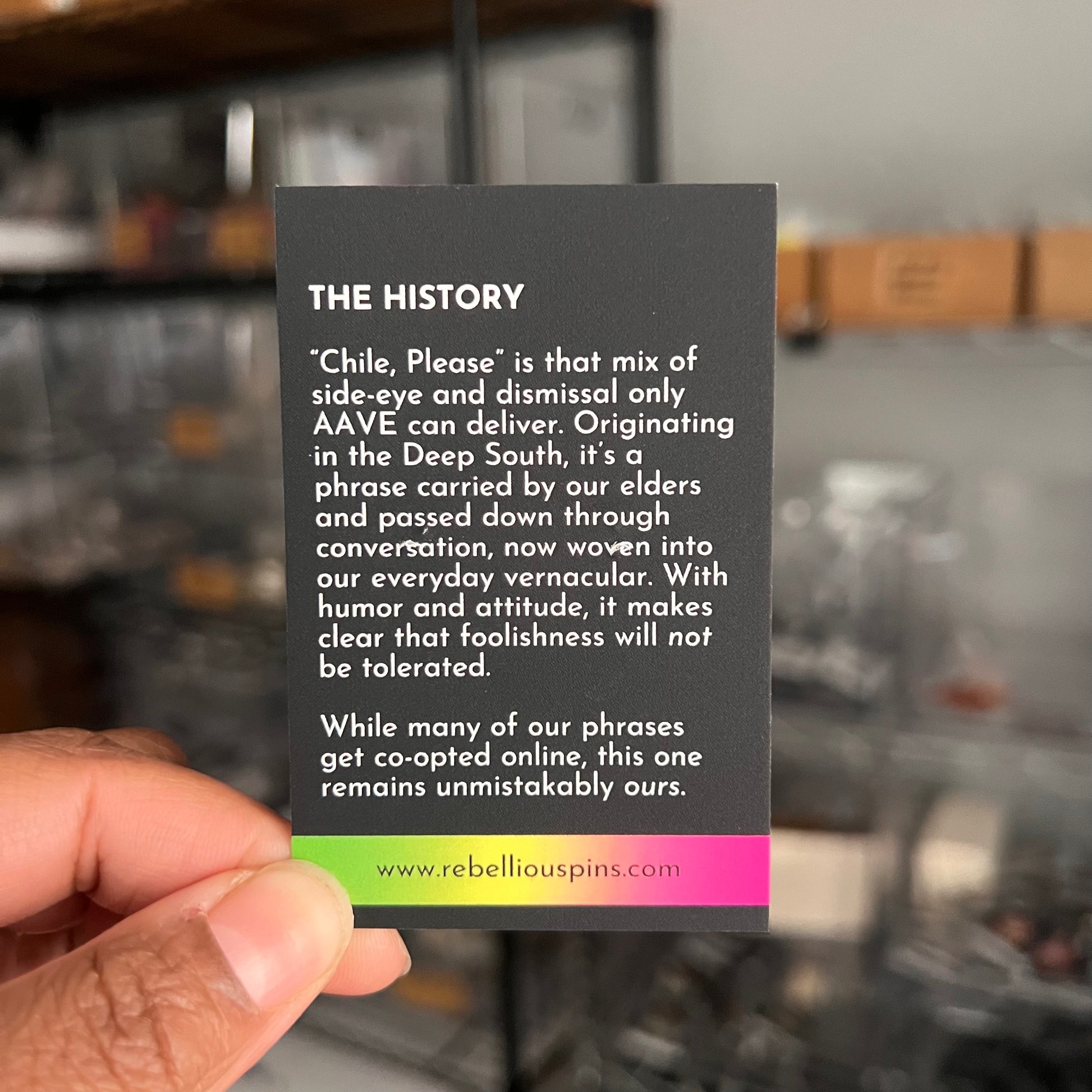 Card with text about 'Chile, Please' phrase held by a hand in a blurred indoor setting.