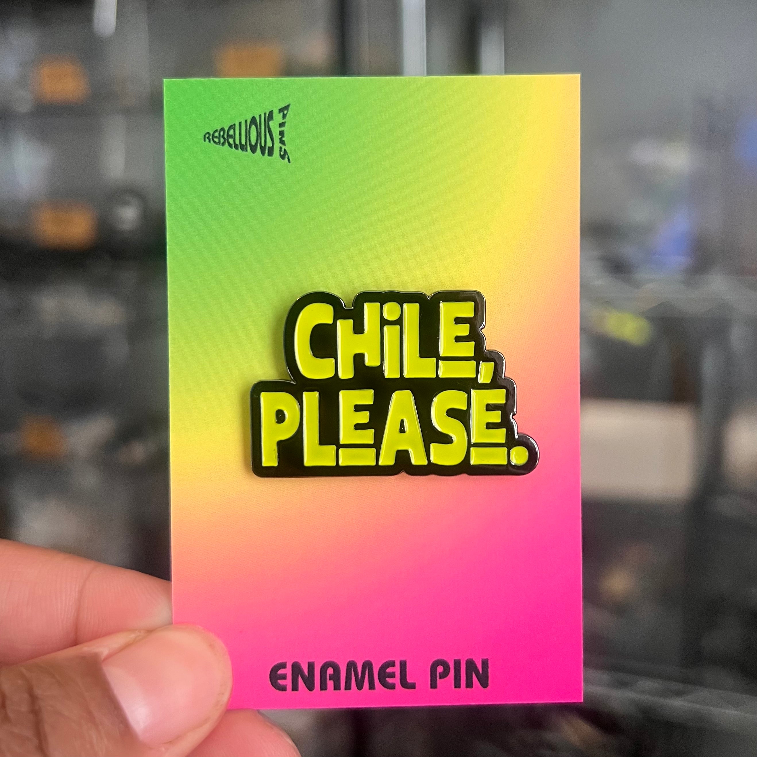 Enamel pin with 'Chile, Please' text on a gradient card held by a hand.