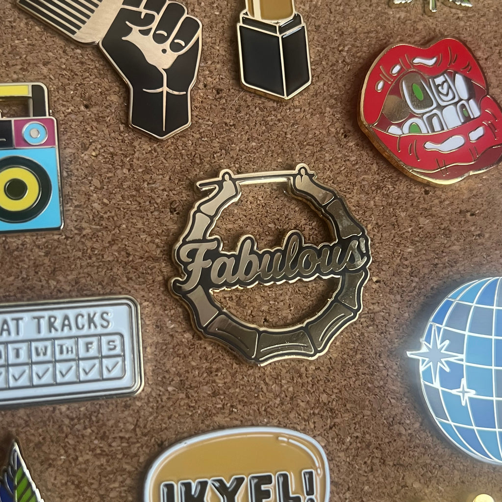 Collection of various pins on a cork board with 'Fabulous' pin prominently displayed.