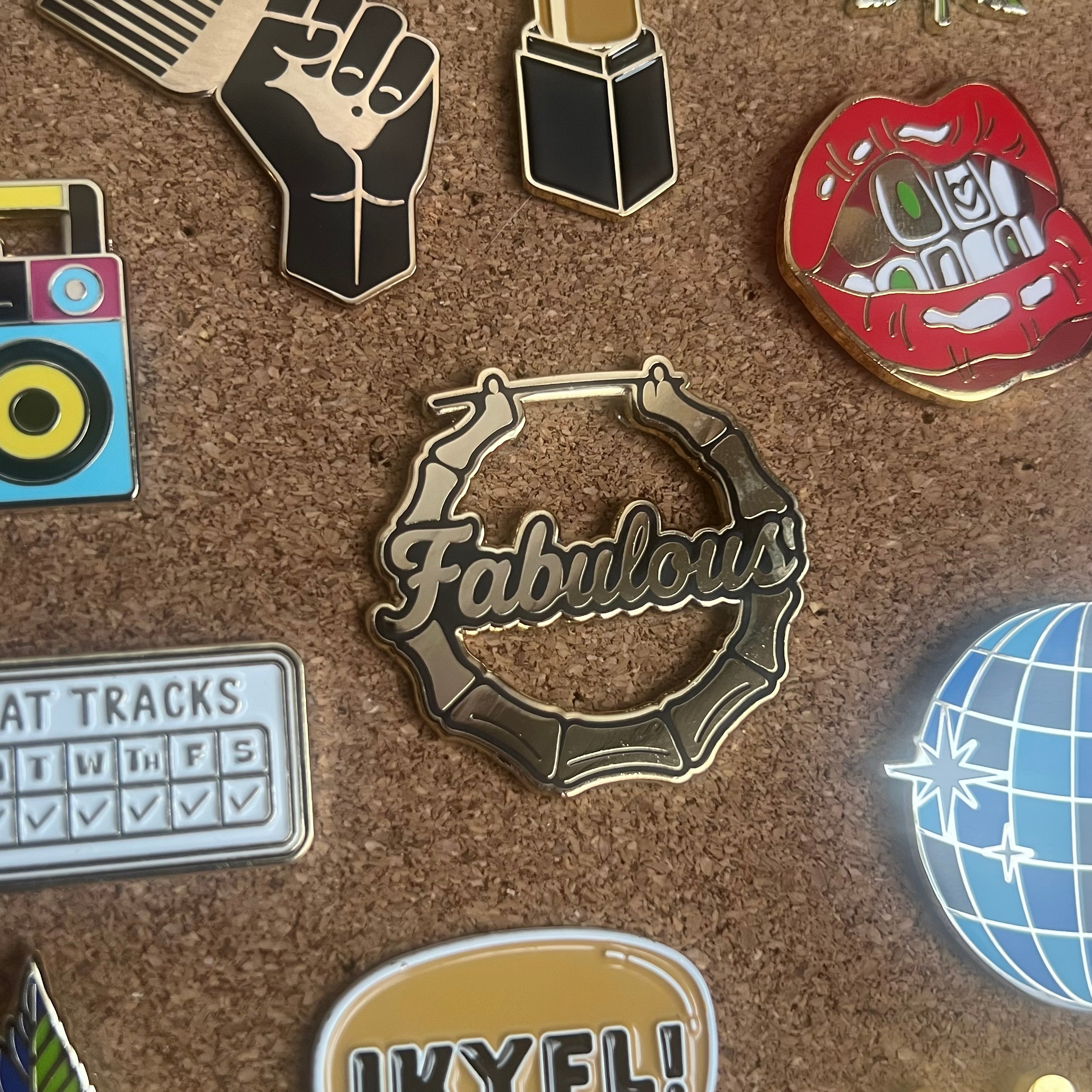 Collection of various pins on a cork board with 'Fabulous' pin prominently displayed.