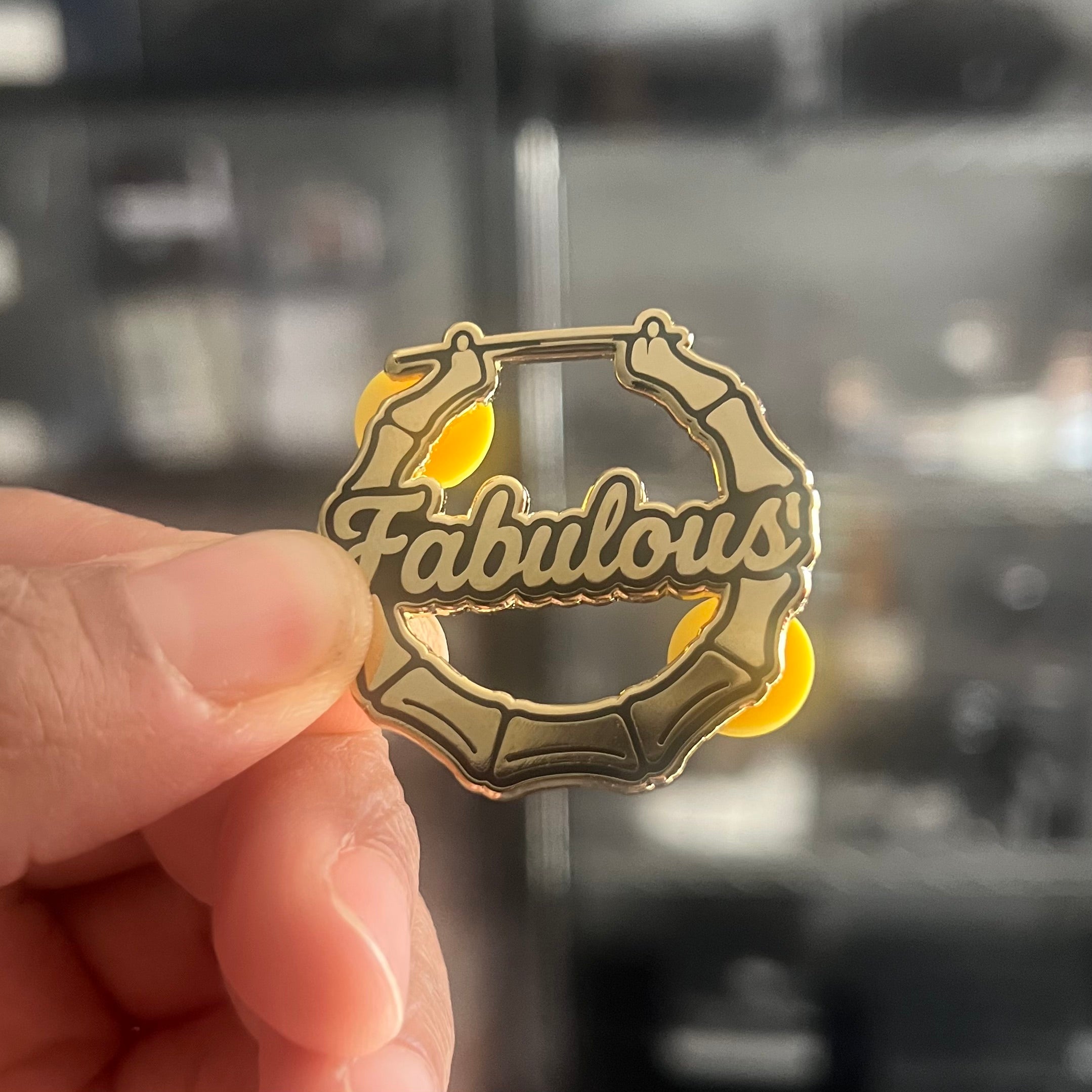 Gold 'Fabulous' badge held by a hand with a blurred background