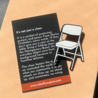 Folding chair enamel pin with descriptive text on a cardboard background