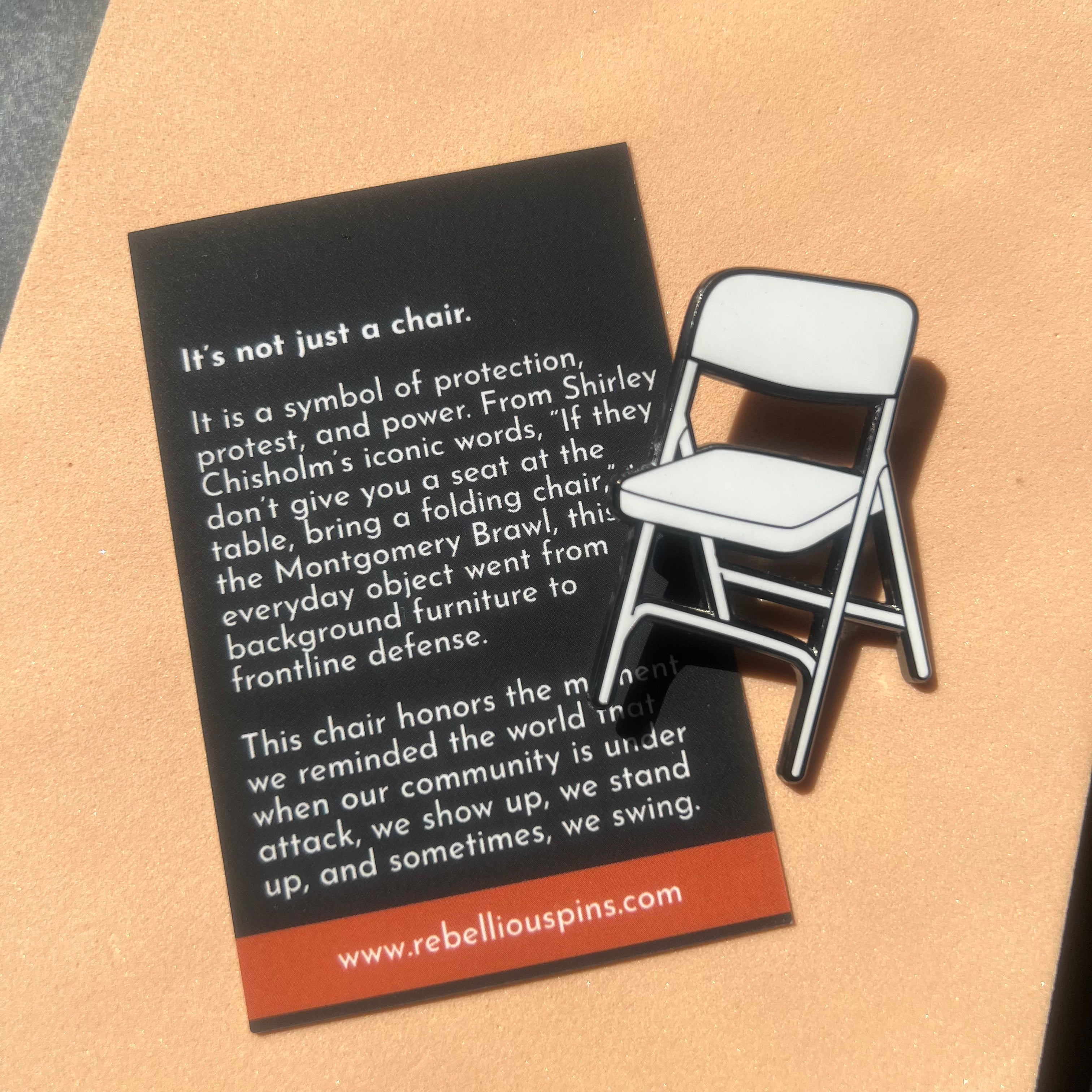 Folding chair enamel pin with descriptive text on a cardboard background