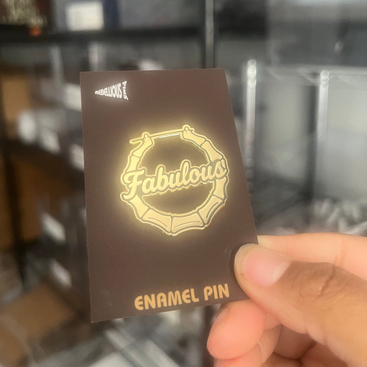 Card with 'Fabulous' enamel pin design held by a hand against a blurred background