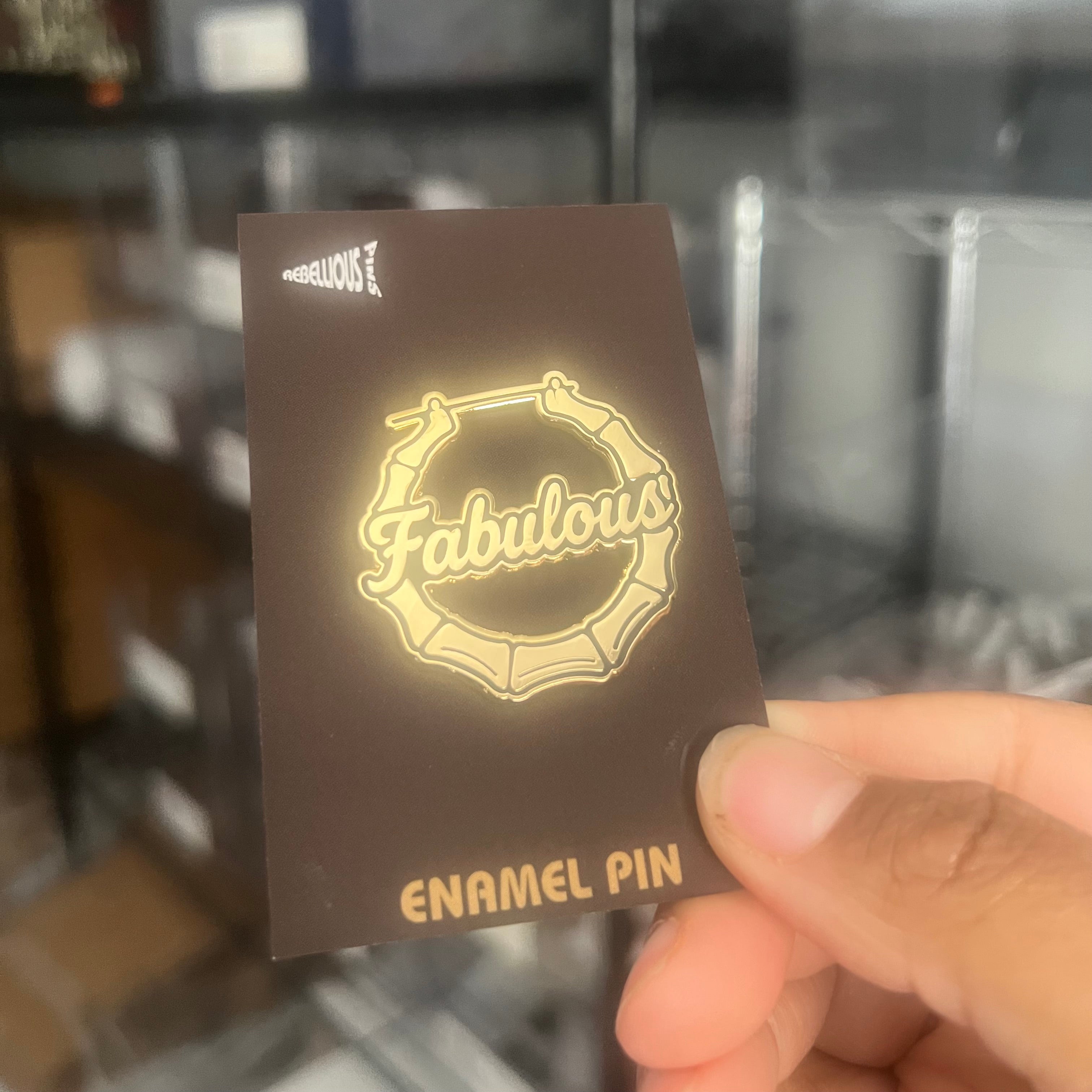 Card with 'Fabulous' enamel pin design held by a hand against a blurred background