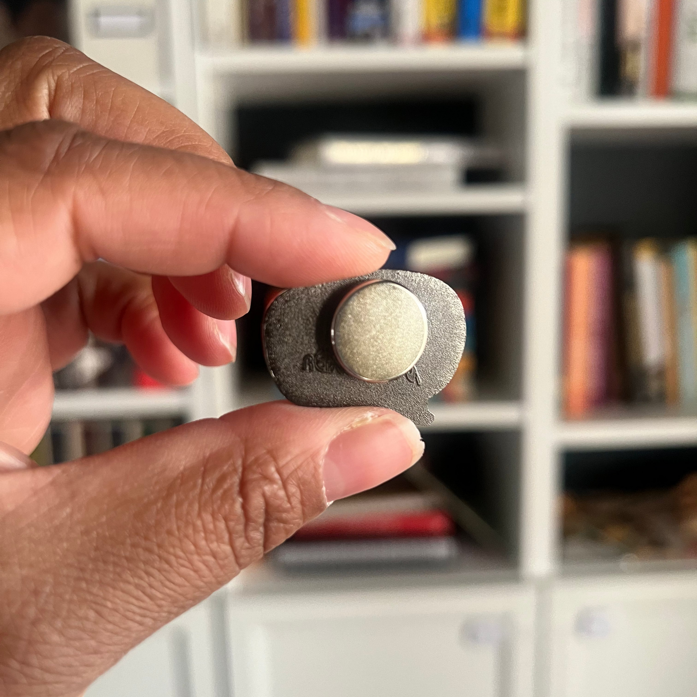 Hand holding a small magnet pin  against a blurred bookshelf background