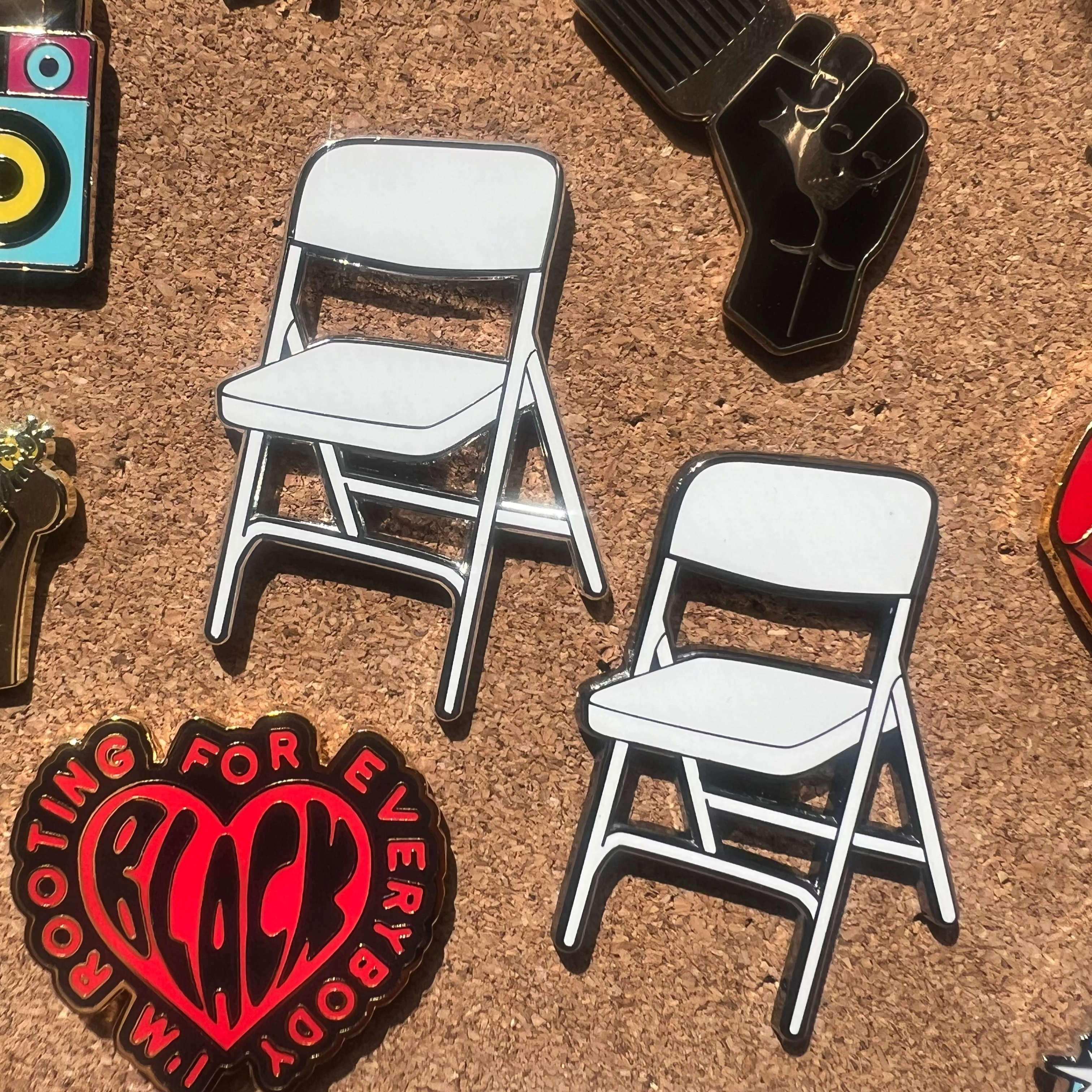 Collection of pins including a chair, heart with text, and other designs on a cork board.