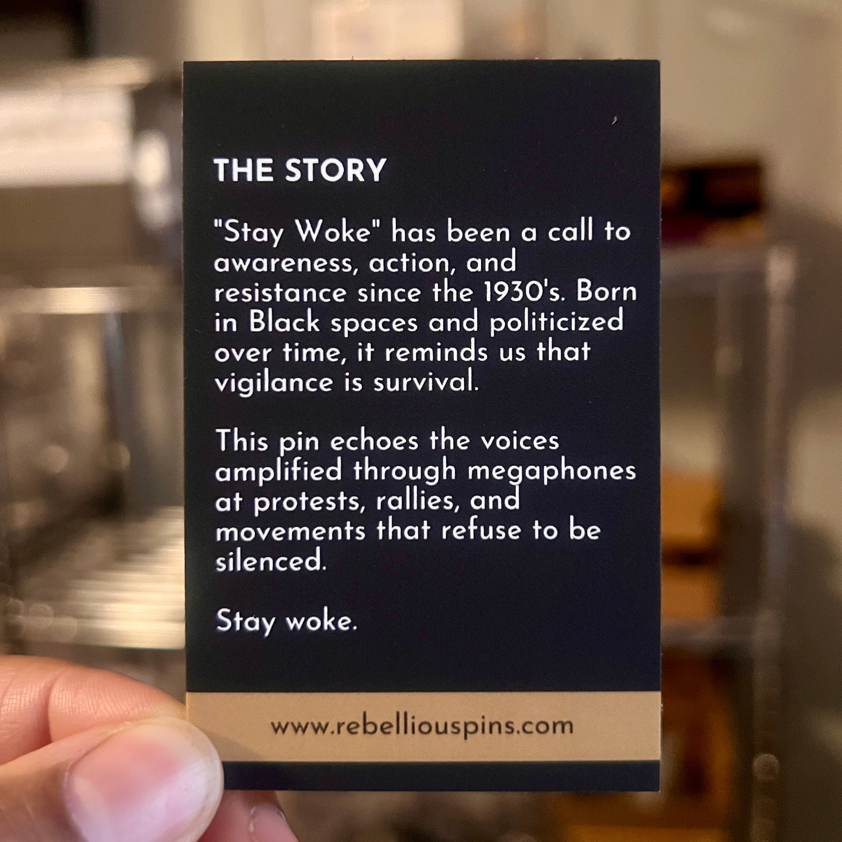 Card with text about 'Stay Woke' movement held by a hand, with a blurred background.
