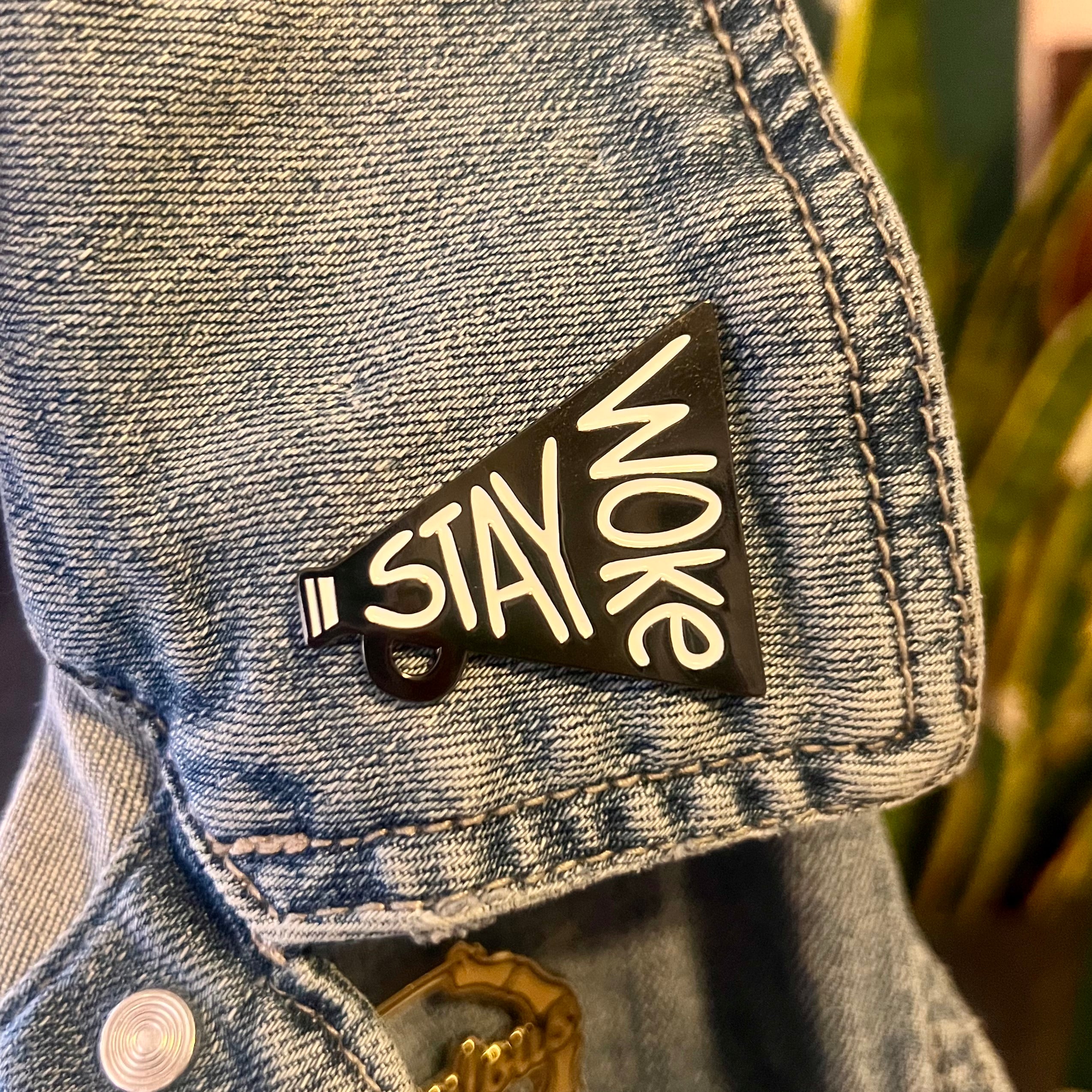 Denim jacket with a 'Stay Woke' pin on a blurred background