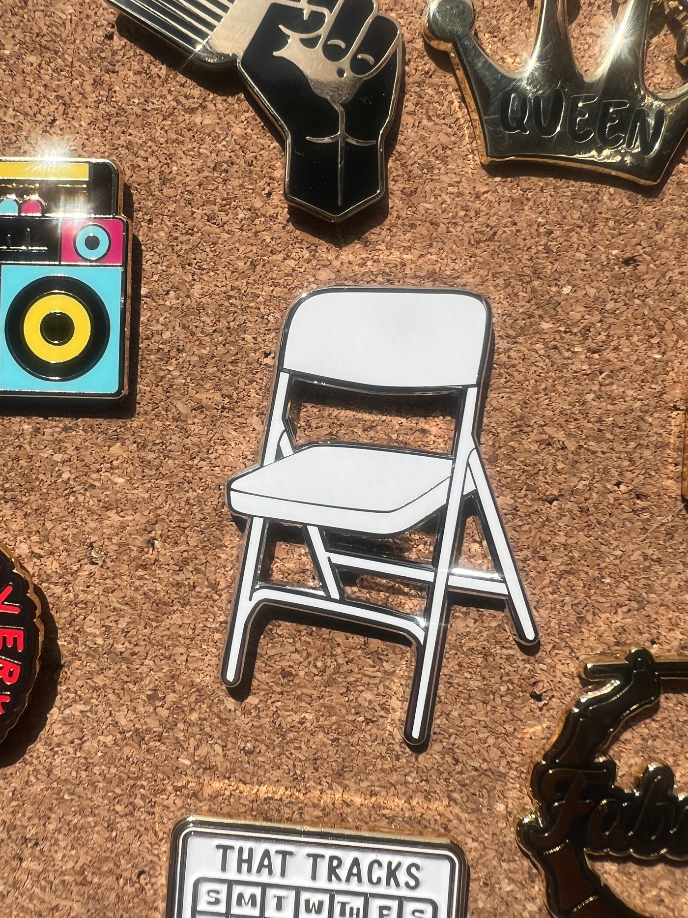 Pin with a white folding chair design on a cork board with other pins.