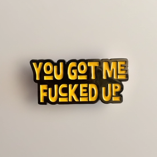 Metallic badge with text 'YOU GOT ME FUCKED UP' on a beige background