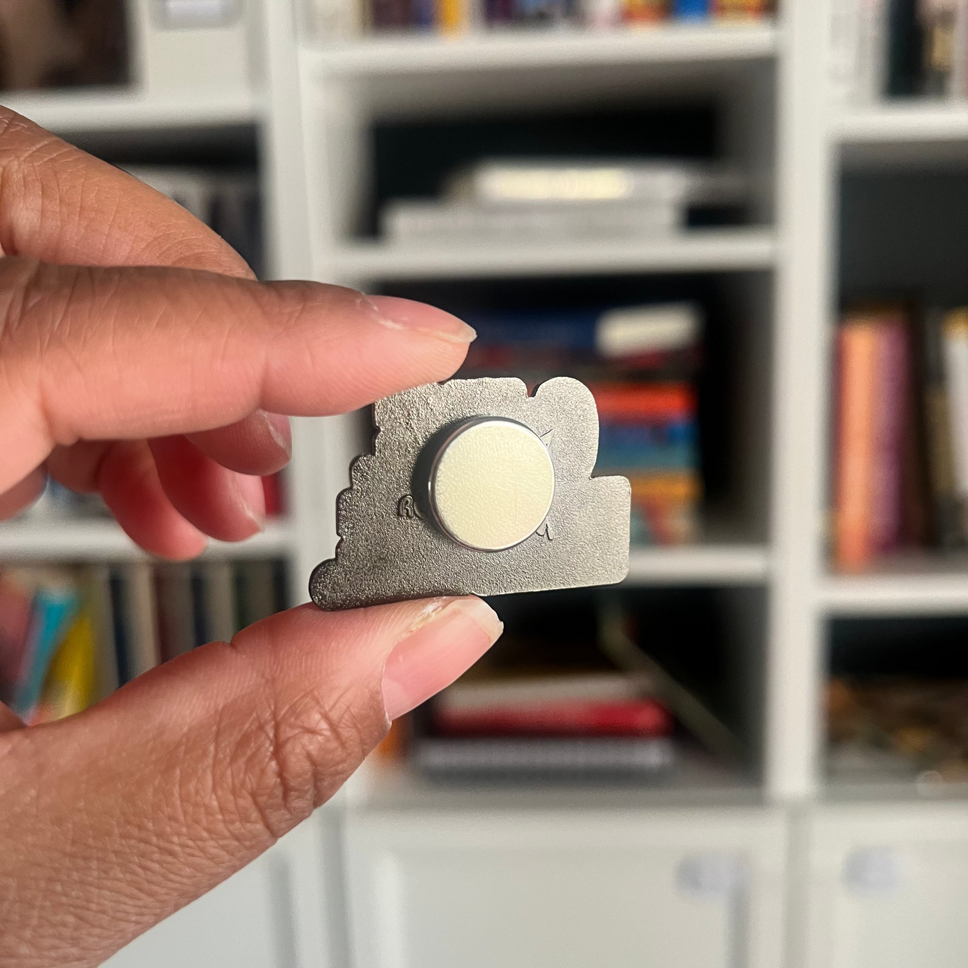 hand holding a magnet enamel pin showing the back magnet. 