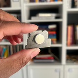 hand holding a magnet enamel pin showing the back magnet. 