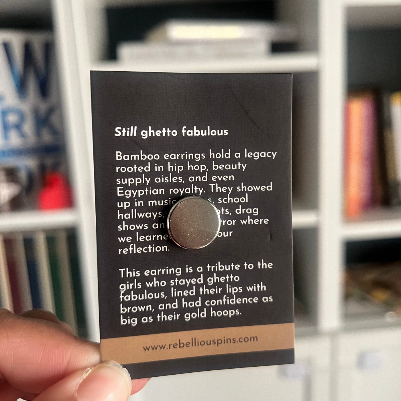 Card with text for magnet enamel pin design in front of a bookshelf.