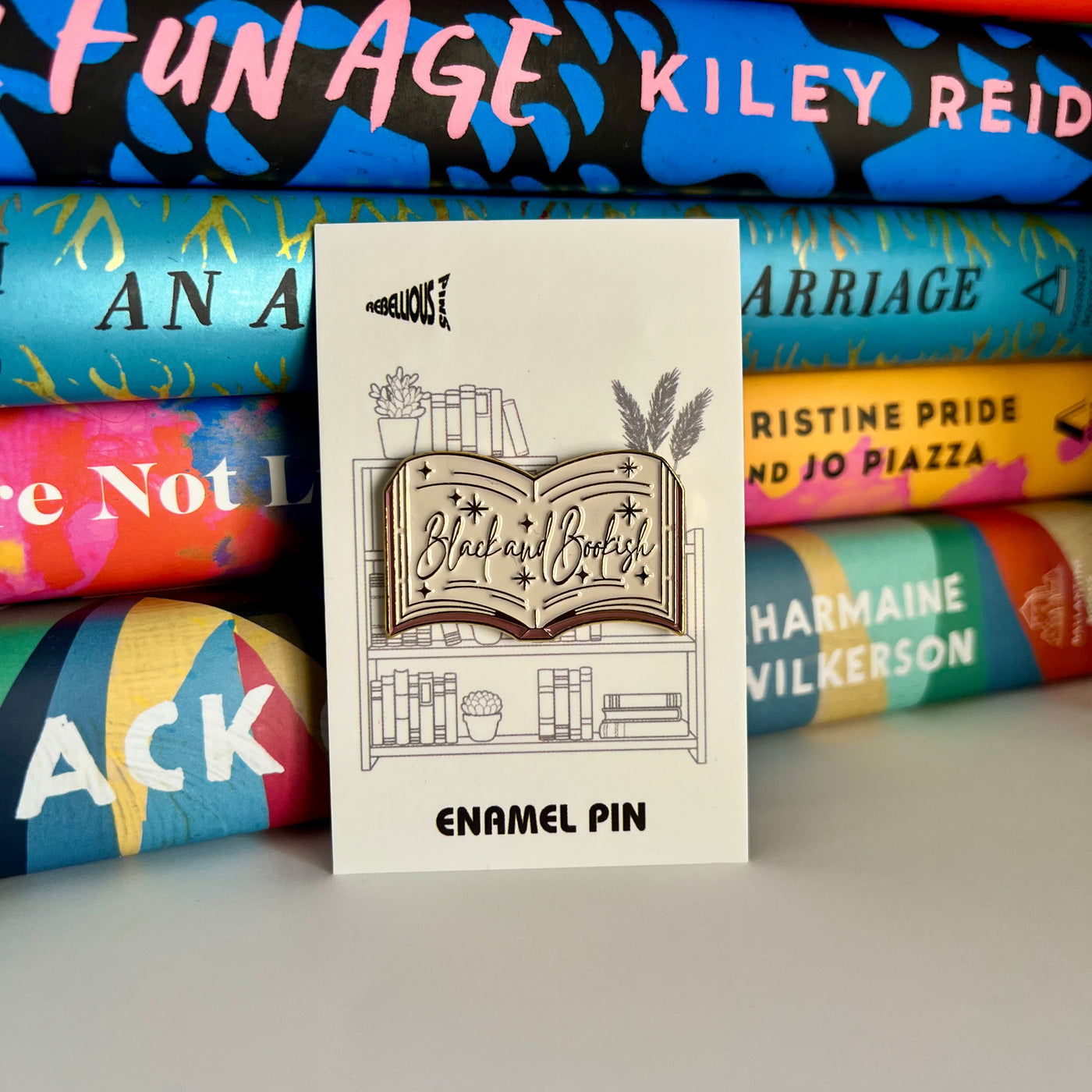 Enamel pin with book design in front of colorful books