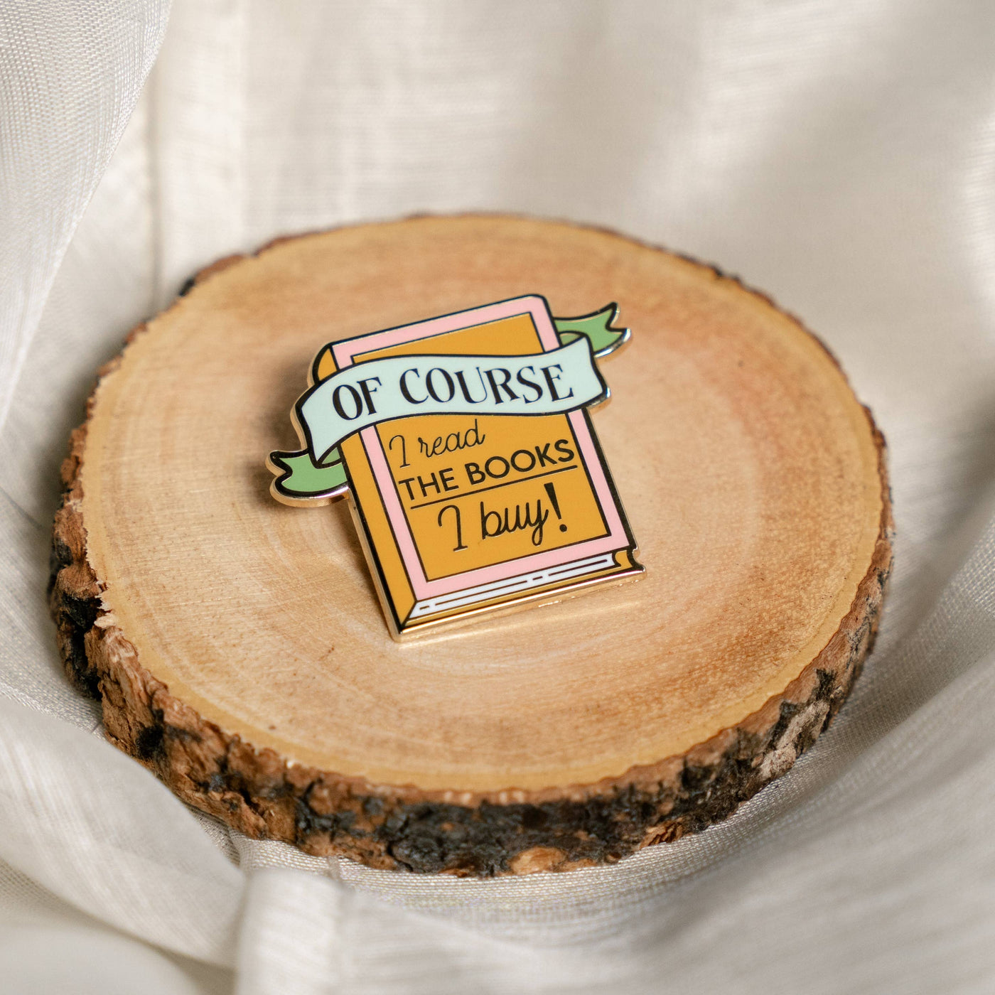 Wooden coaster with a book-themed pin on a white fabric background
