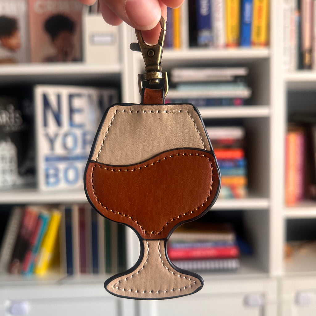 Leather keychain shaped like a wine glass held in front of a bookshelf.