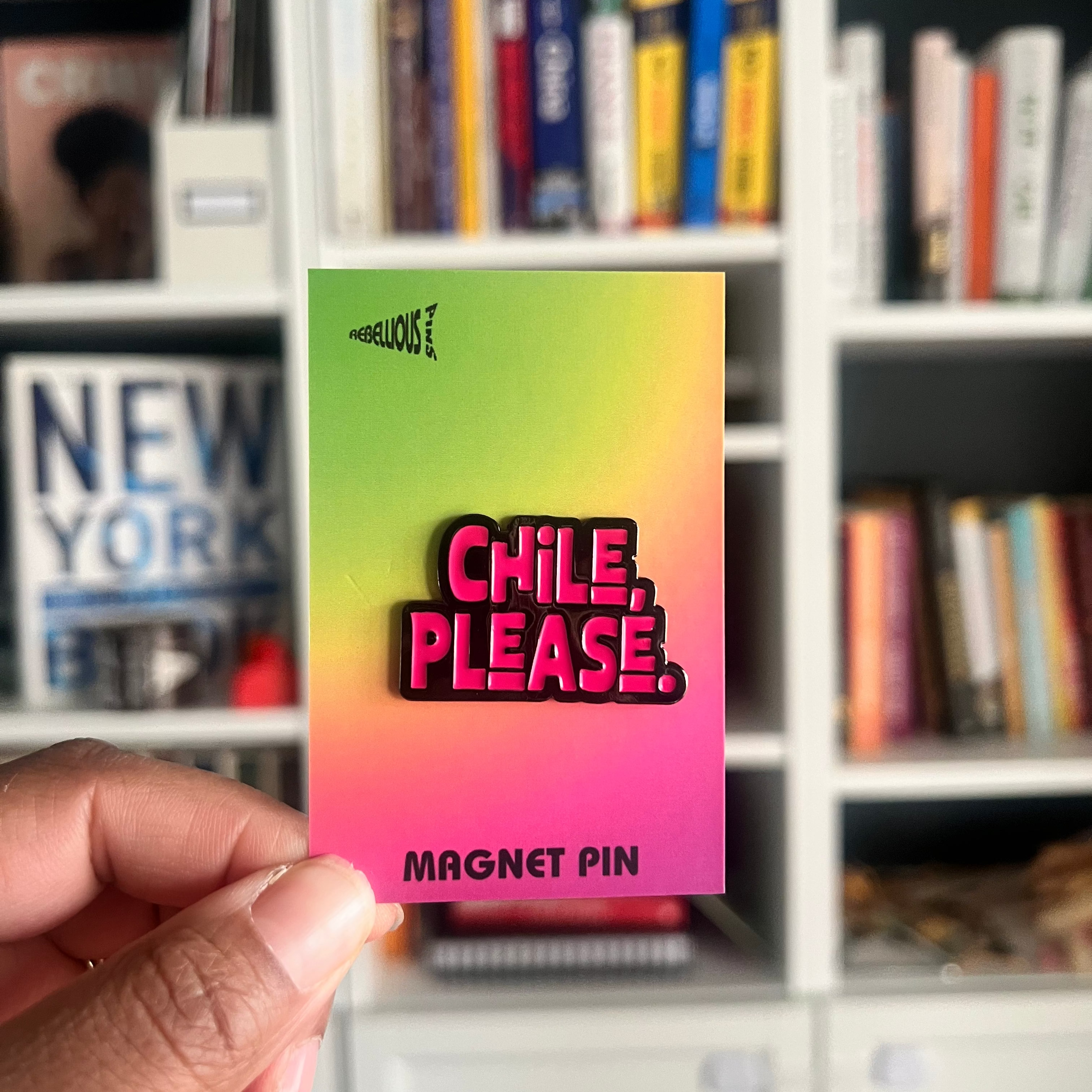 Card with 'Chile, Please' magnet pin design held in front of a bookshelf.