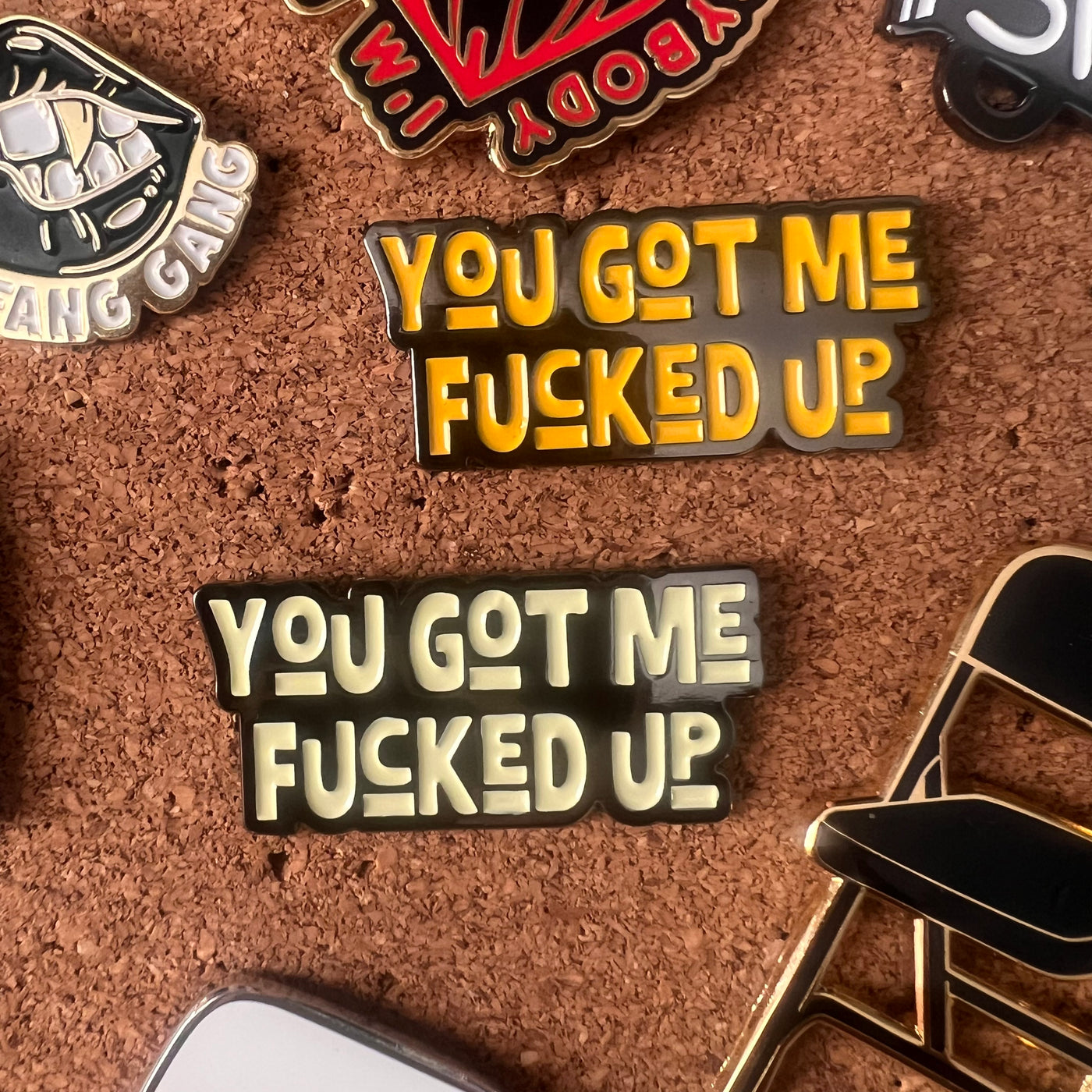 Two pins with the text 'YOU GOT ME FUCKED UP' on a cork board background.