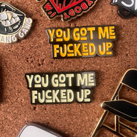 Two pins with the text 'YOU GOT ME FUCKED UP' on a cork board background.