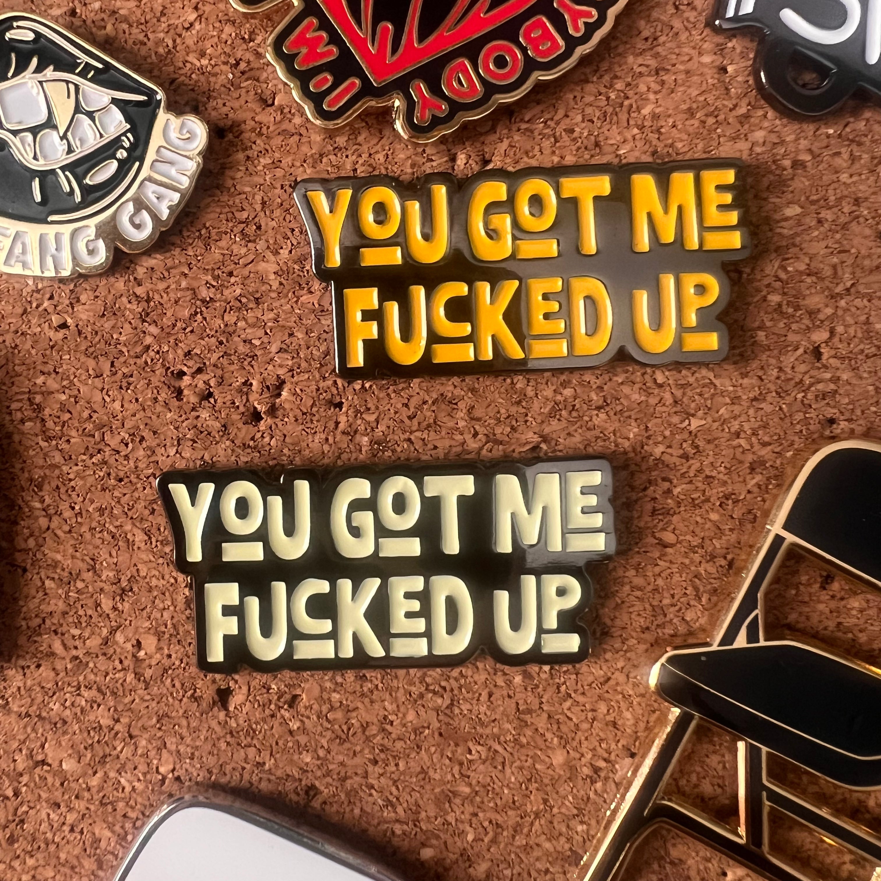 Two pins with the text 'YOU GOT ME FUCKED UP' on a cork board background.